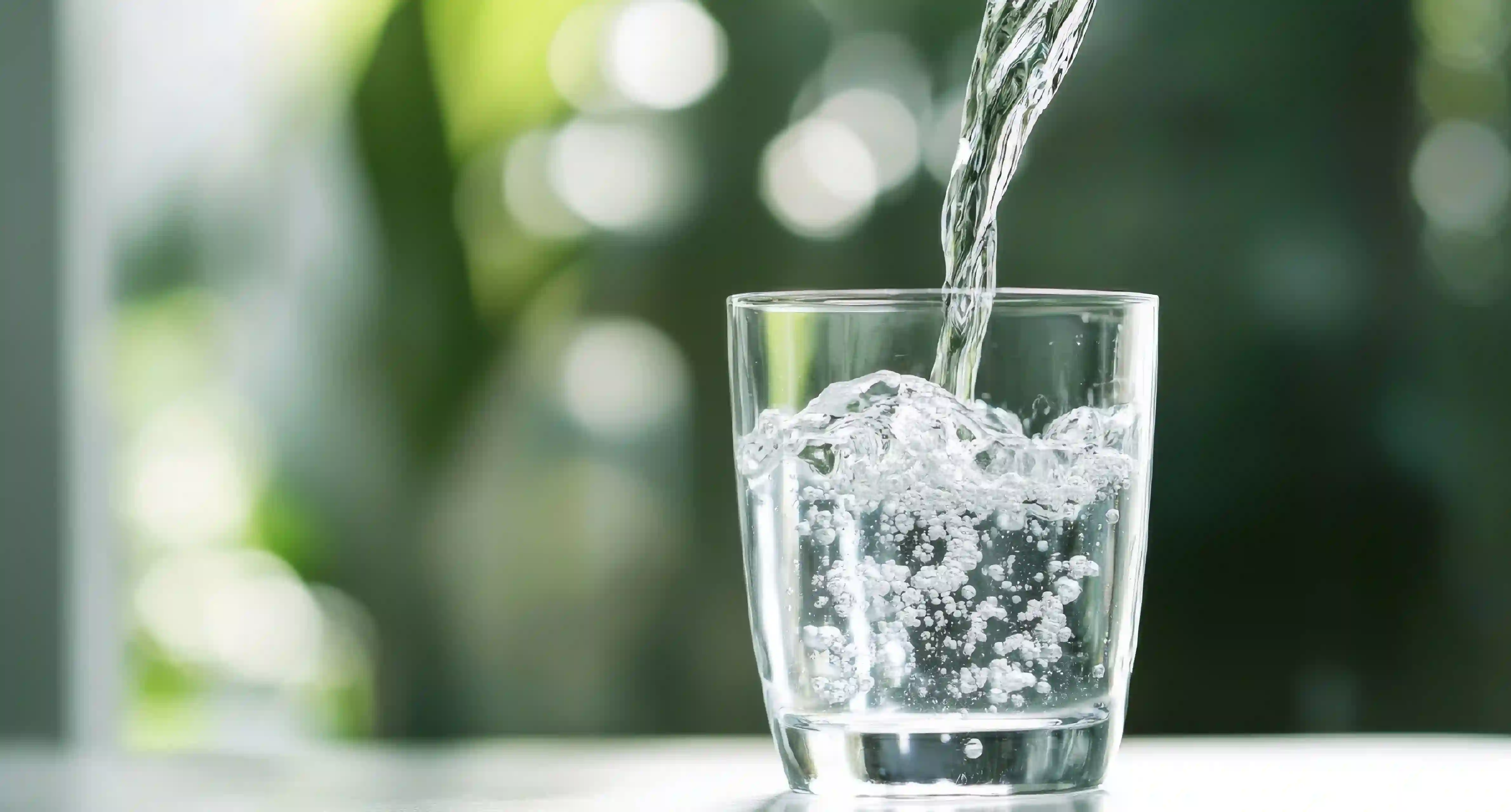 Pouring water in a glass with a blurred outdoors background