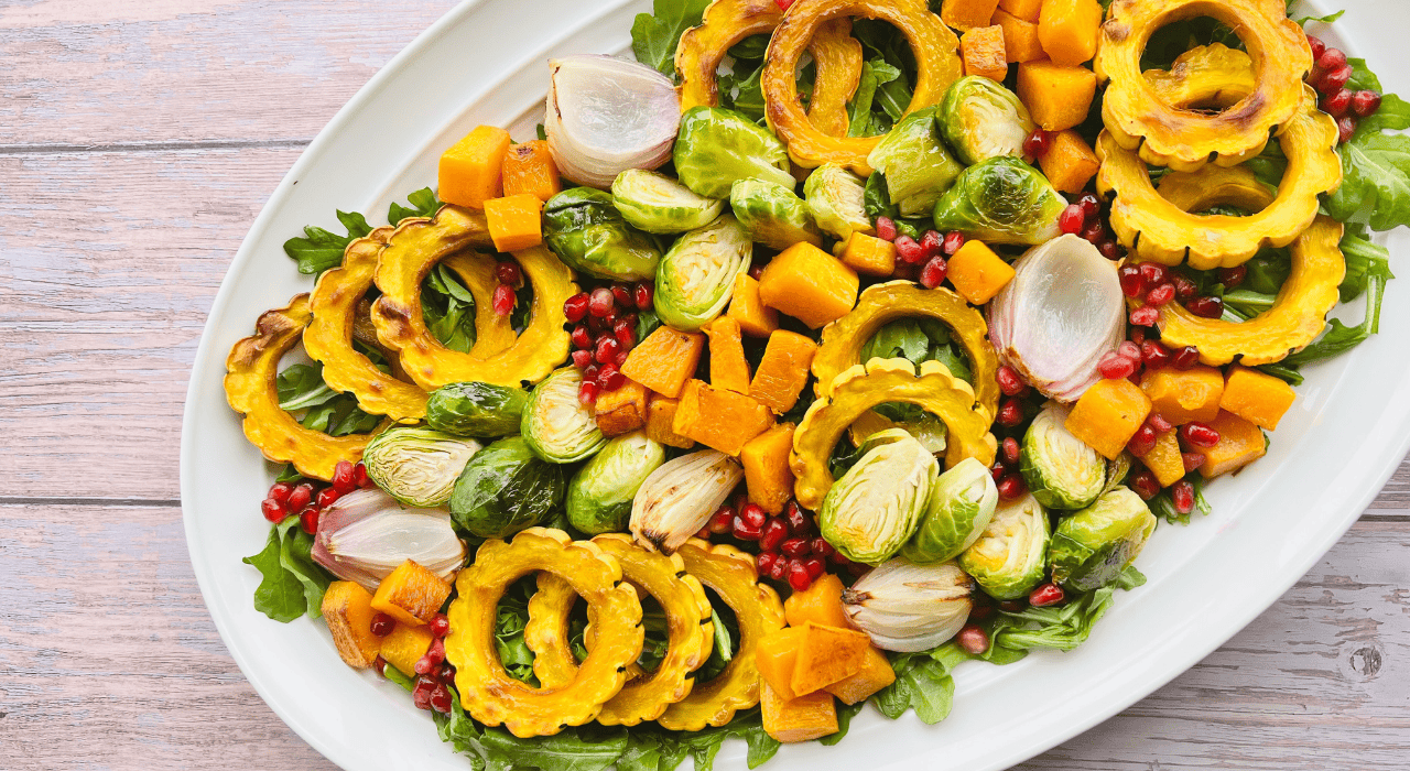 A vibrant fall salad featuring roasted golden squash, Brussel sprouts, and fresh arugula, served in a white bowl.