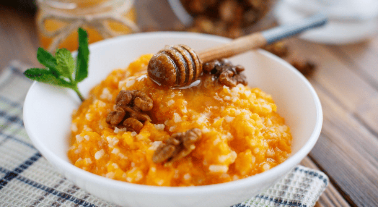 A lovely pumpkin orange millet porridge in a white bowl, topped with honey and walnuts