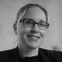 Smiling woman wearing glasses and a dark blazer, with hair pulled back.