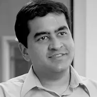 Portrait of a smiling man with dark hair wearing a collared shirt in an indoor setting.