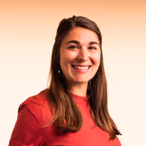 Vrouw met lang bruin haar en rode trui die glimlacht voor een lichte achtergrond.