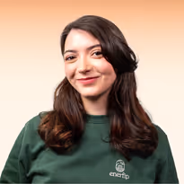 Vrouw met lang donker haar en groene trui met logo, glimlachend tegen een lichte achtergrond.