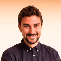 Man met kort, donker haar en baard glimlacht en draagt een zwarte button-up shirt.