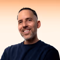 Gladde man met kort donker haar en baard glimlacht zwart trui dragend tegen een lichte achtergrond.