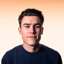 Jonge man met kort donker haar en een donkerblauw shirt tegen een lichte, oranje achtergrond.