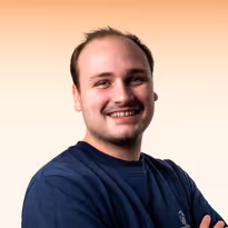 Jonge man met kort haar en lichte baard lacht met gekruiste armen, scherp tegen een effen lichte achtergrond.