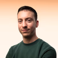 Portret van een man met kort bruin haar en groene trui, glimlachend voor een lichte achtergrond.