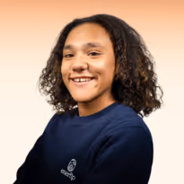 Jong persoon met krullend haar draagt donkerblauw shirt en glimlacht tegen een lichte achtergrond.