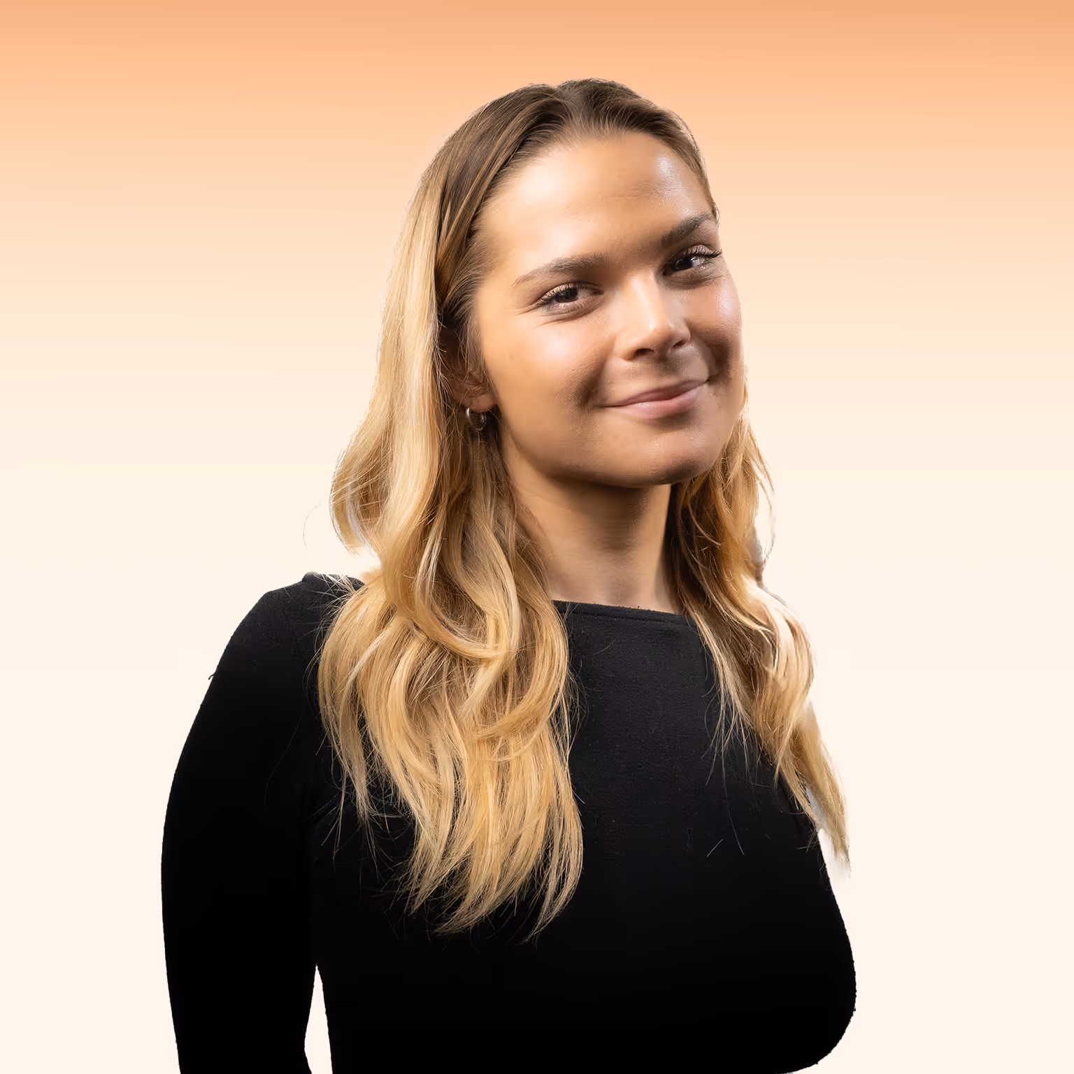 Vrouw met lang blond haar en zwarte trui lachend voor een oranje-witte achtergrond.