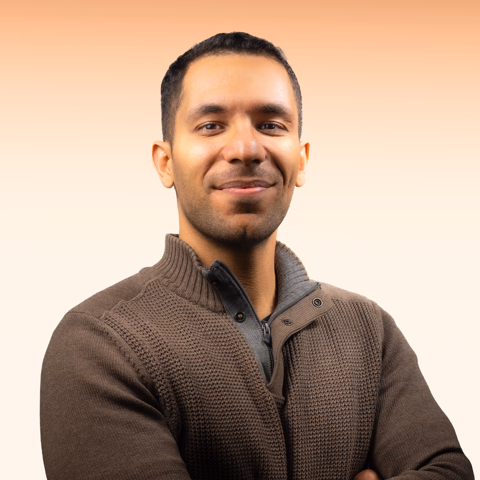 Man met kort zwart haar en een bruine gebreide trui kijkt zelfverzekerd met lichte glimlach.
