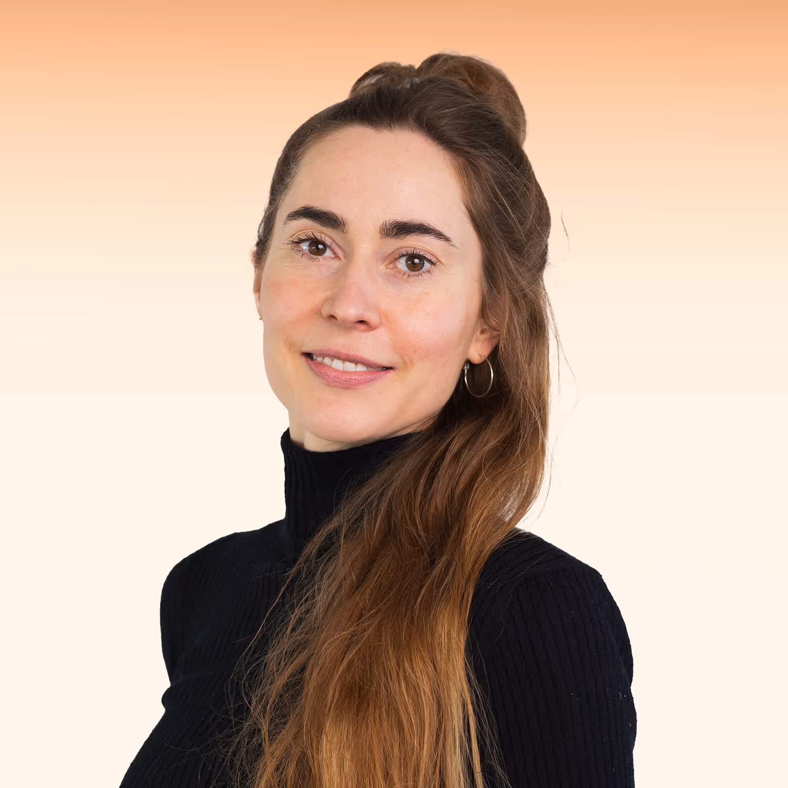 Vrouw met lang bruin haar in een zwarte coltrui, glimlachend voor een verloopachtergrond van oranje naar crème.