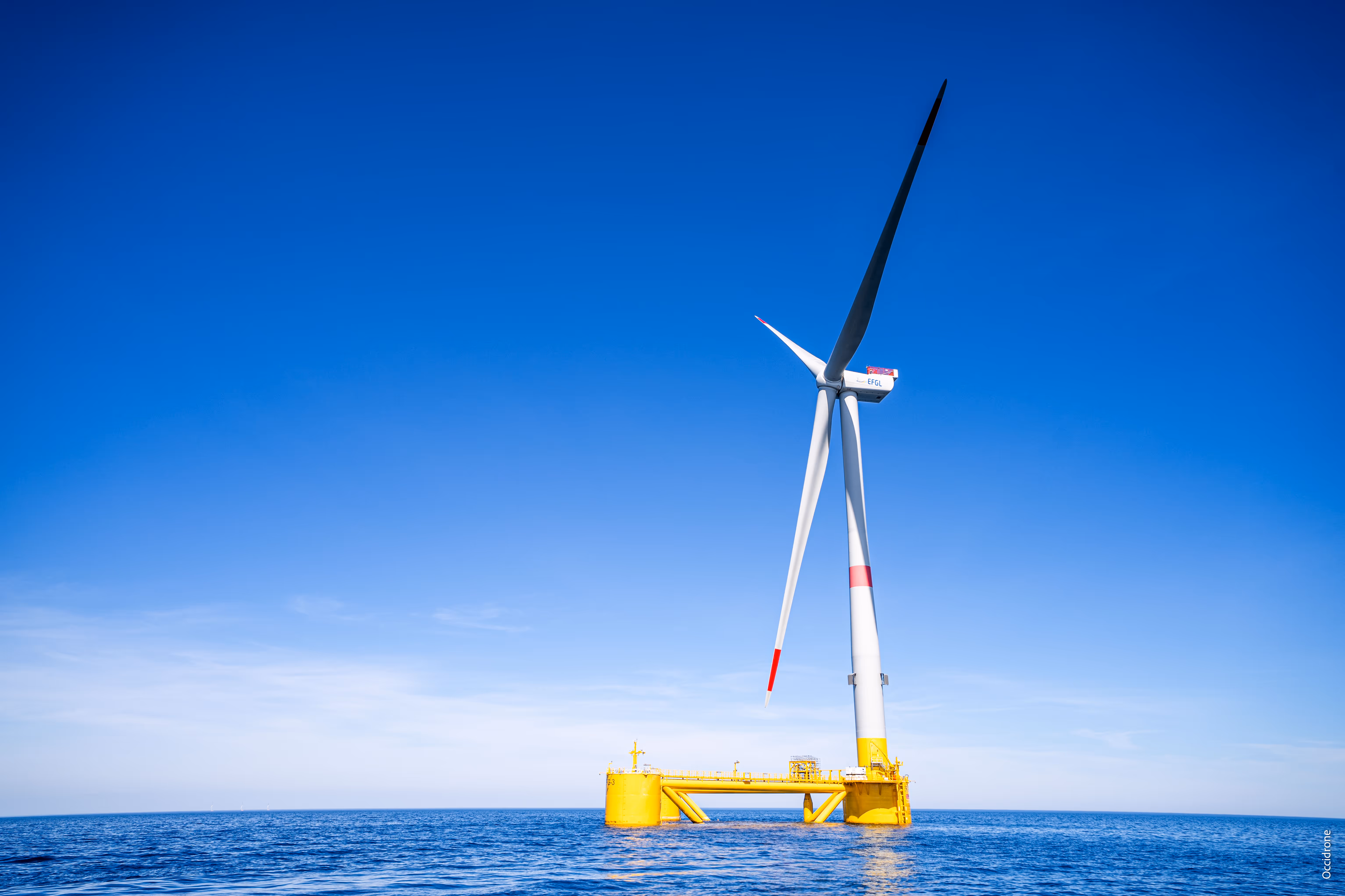 Éolienne offshore avec une fondation flottante jaune dans une mer bleue sous un ciel clair.