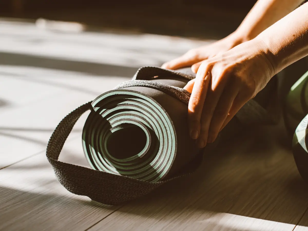 A person rolls up a dark green yoga mat