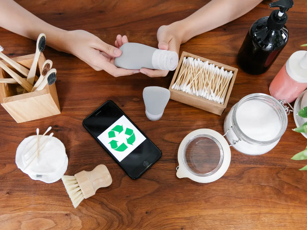 Two hands are going through plastic alternatives, such as a wooden and bamboo scrubbing brush, bamboo toothbrushes, washable cotton pads, and reusable glass jars