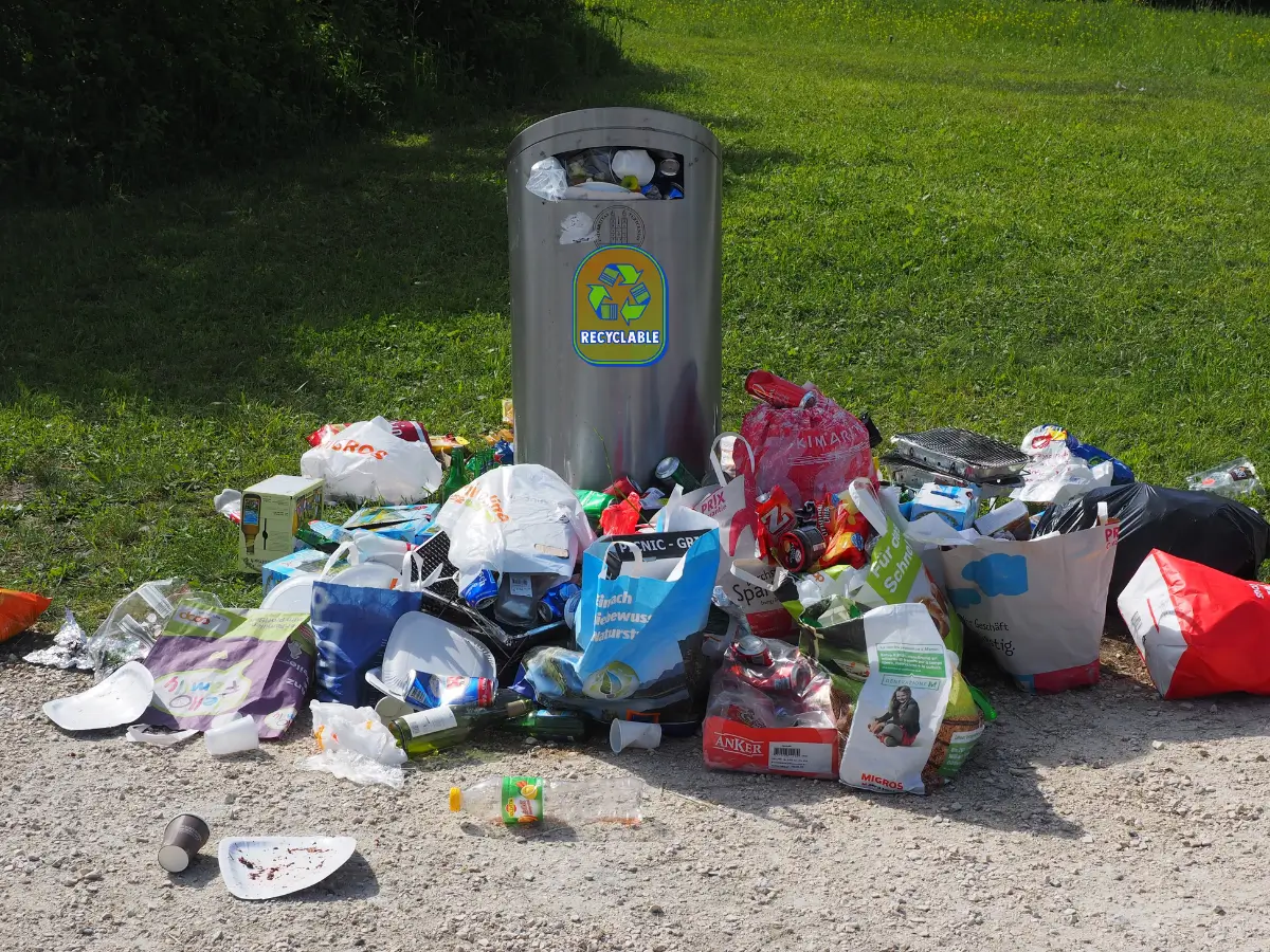 A recycling bin is surrounded by garbage