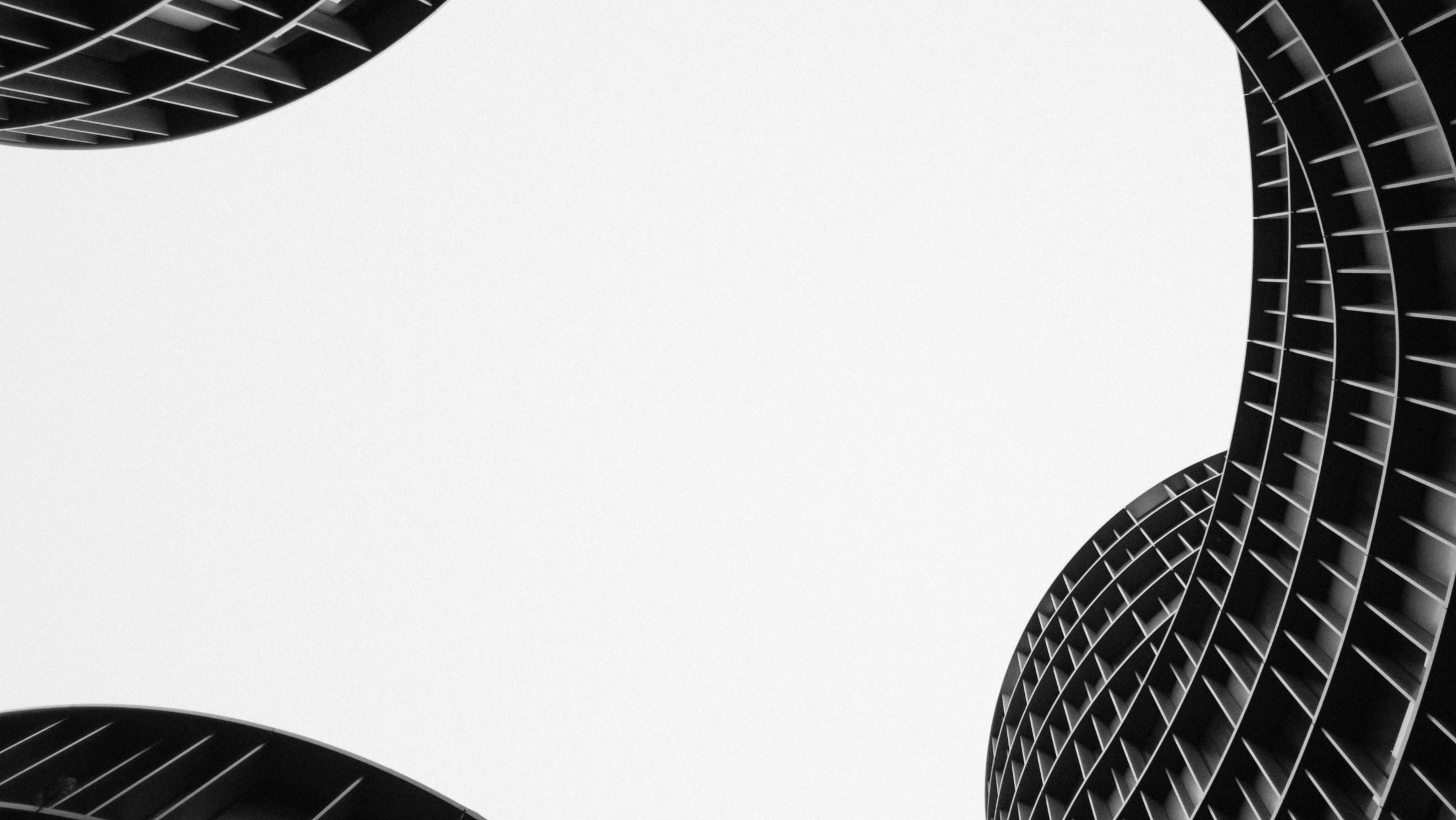 Black and white low-angle view of modern curved buildings with horizontal slats against a bright sky.