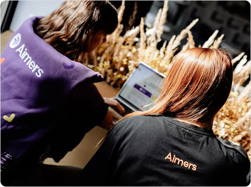 Two people viewed from behind, one wearing a purple vest and the other a black shirt, both with 
