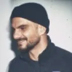 Man in black beanie looking down with serious, intense expression