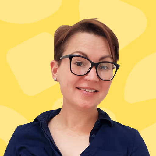 Smiling person with short brown hair and glasses wearing a dark blue shirt against a yellow background.