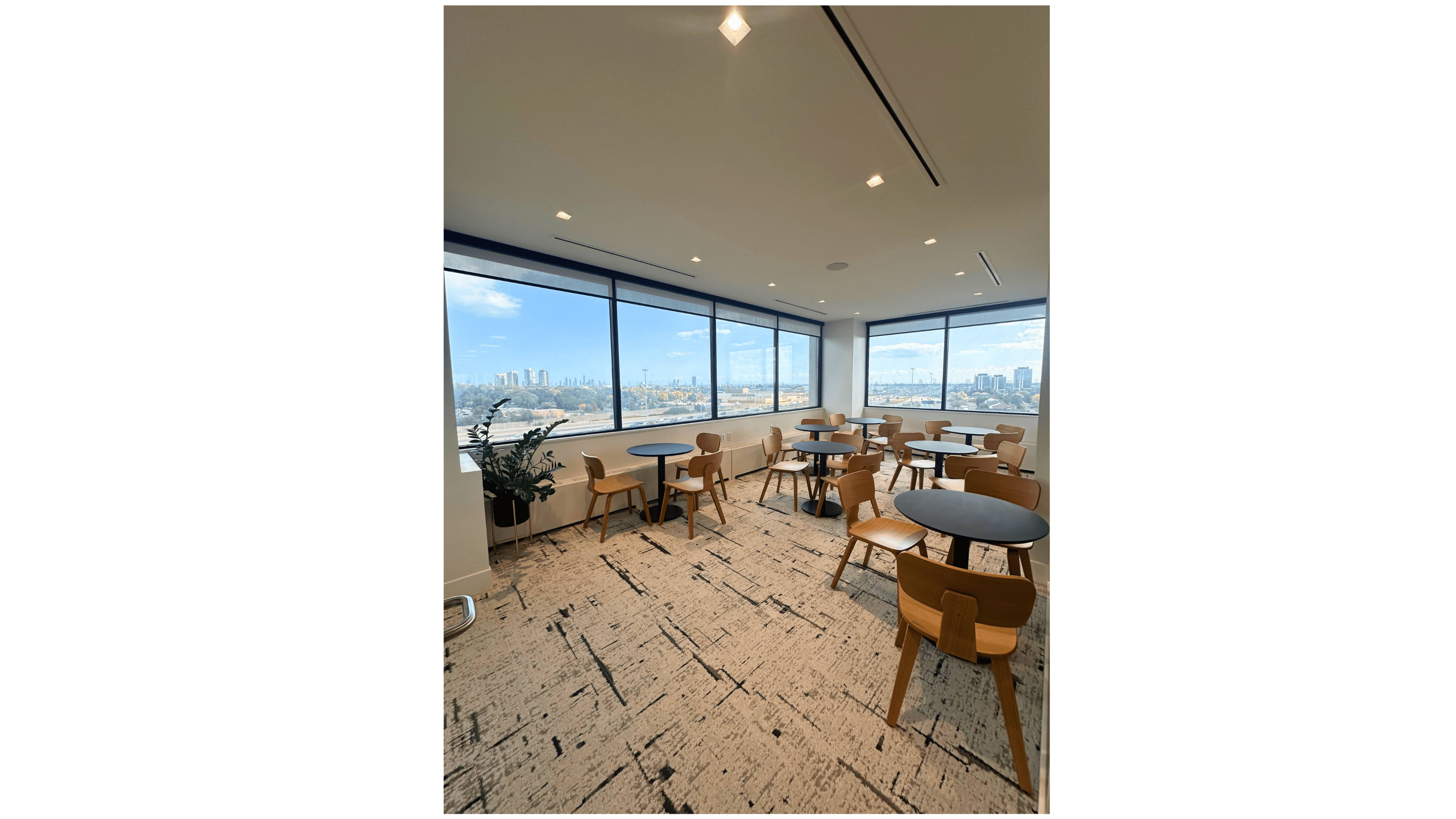 Modern event space with round black tables and wooden chairs, large windows offering a cityscape view.
