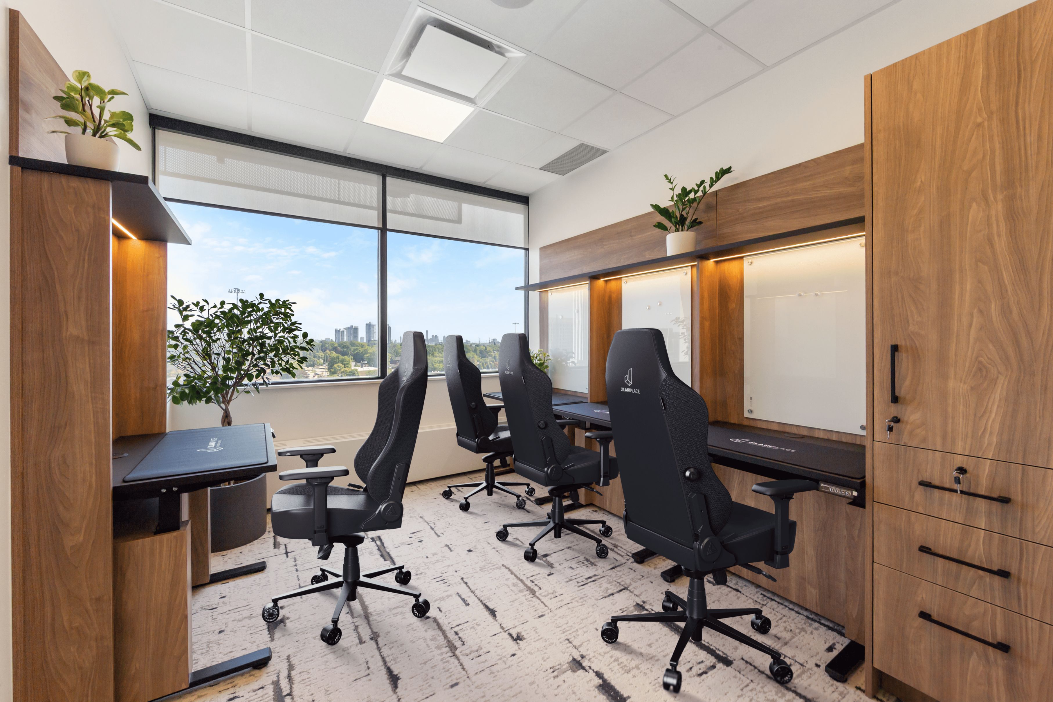 Modern office with four black ergonomic chairs at wooden desks facing large windows with a city view.