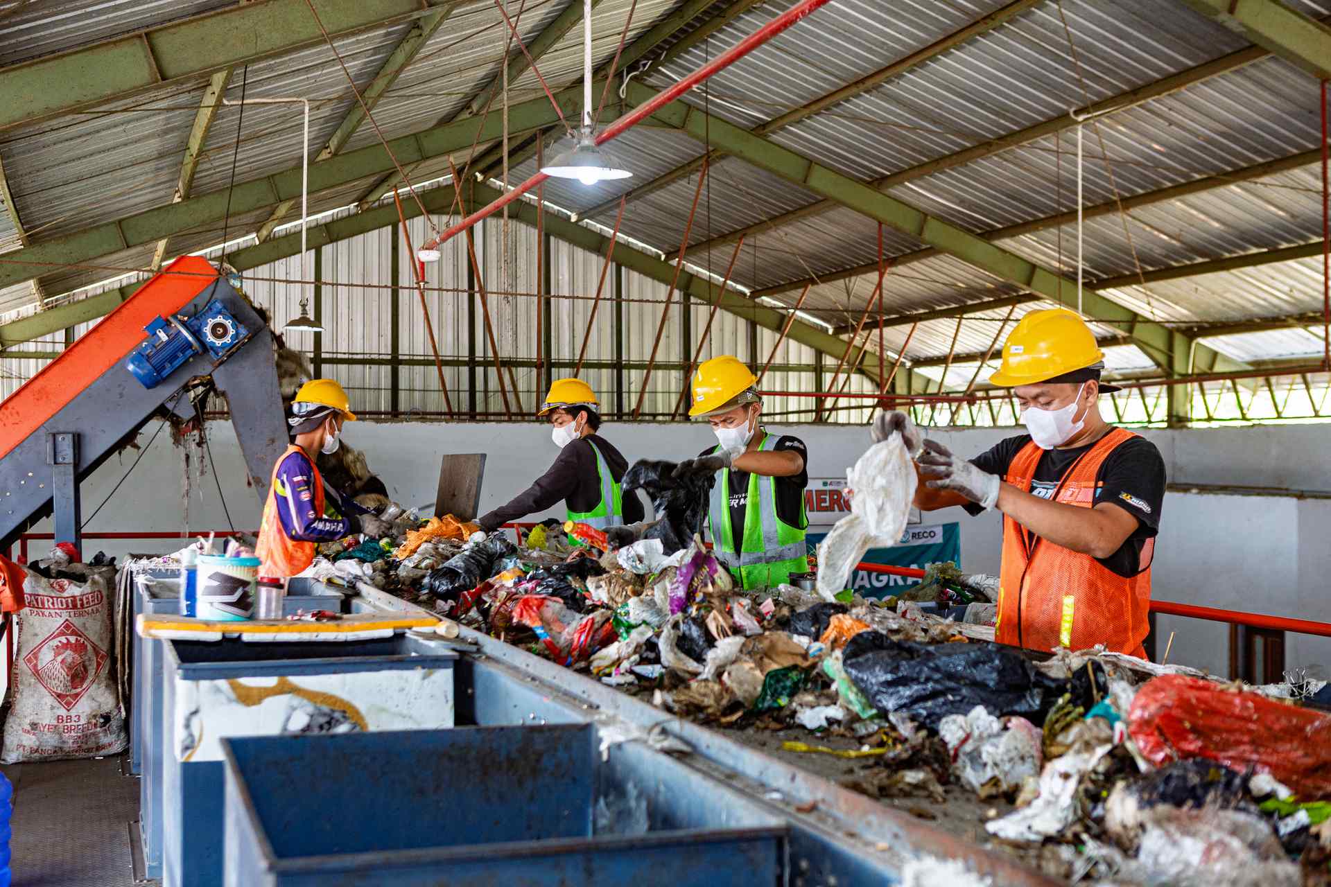 Workers sorting mixed waste on a conveyor at a waste management facility