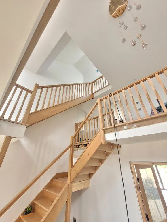 A staircase with a wooden railing, a white wall and feature lighting.