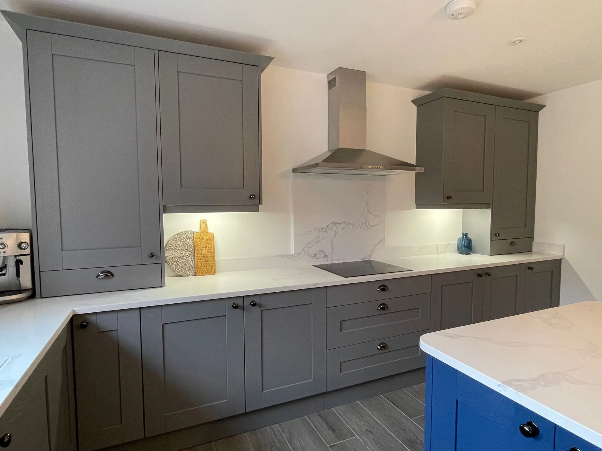 A kitchen with a marble counter top and grey cabinets.
