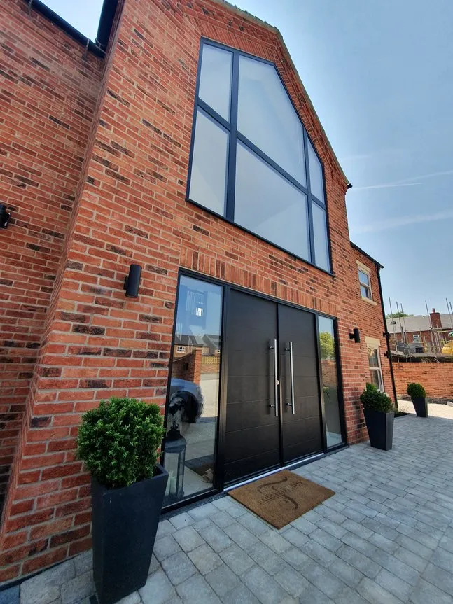A large brick house with a black door, large central window and a green bush in front of it.