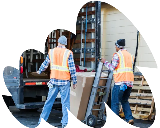 wo workers wearing safety vests and beanies unloading large boxes from a truck using a hand trolley