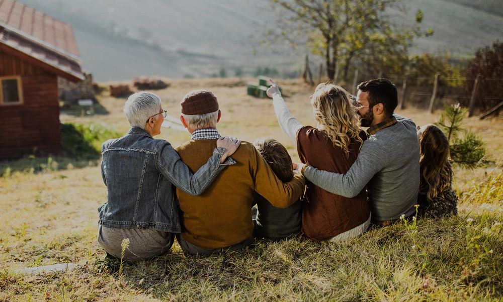 Menschen sitzen am Berghang und schauen auf eine Hütte
