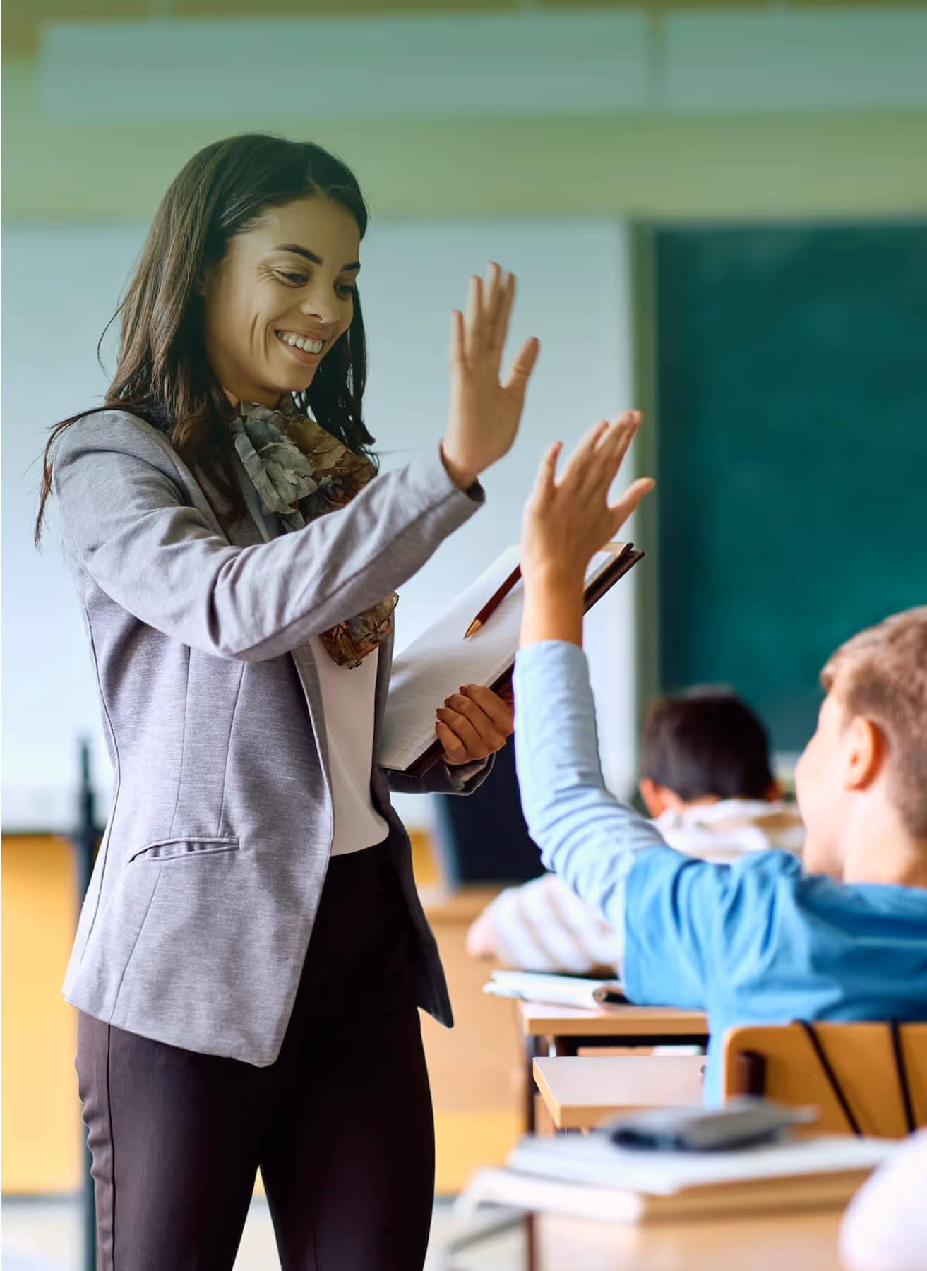 A woman in a classroom shares a joyful moment with a student, giving a high five in celebration of success.
