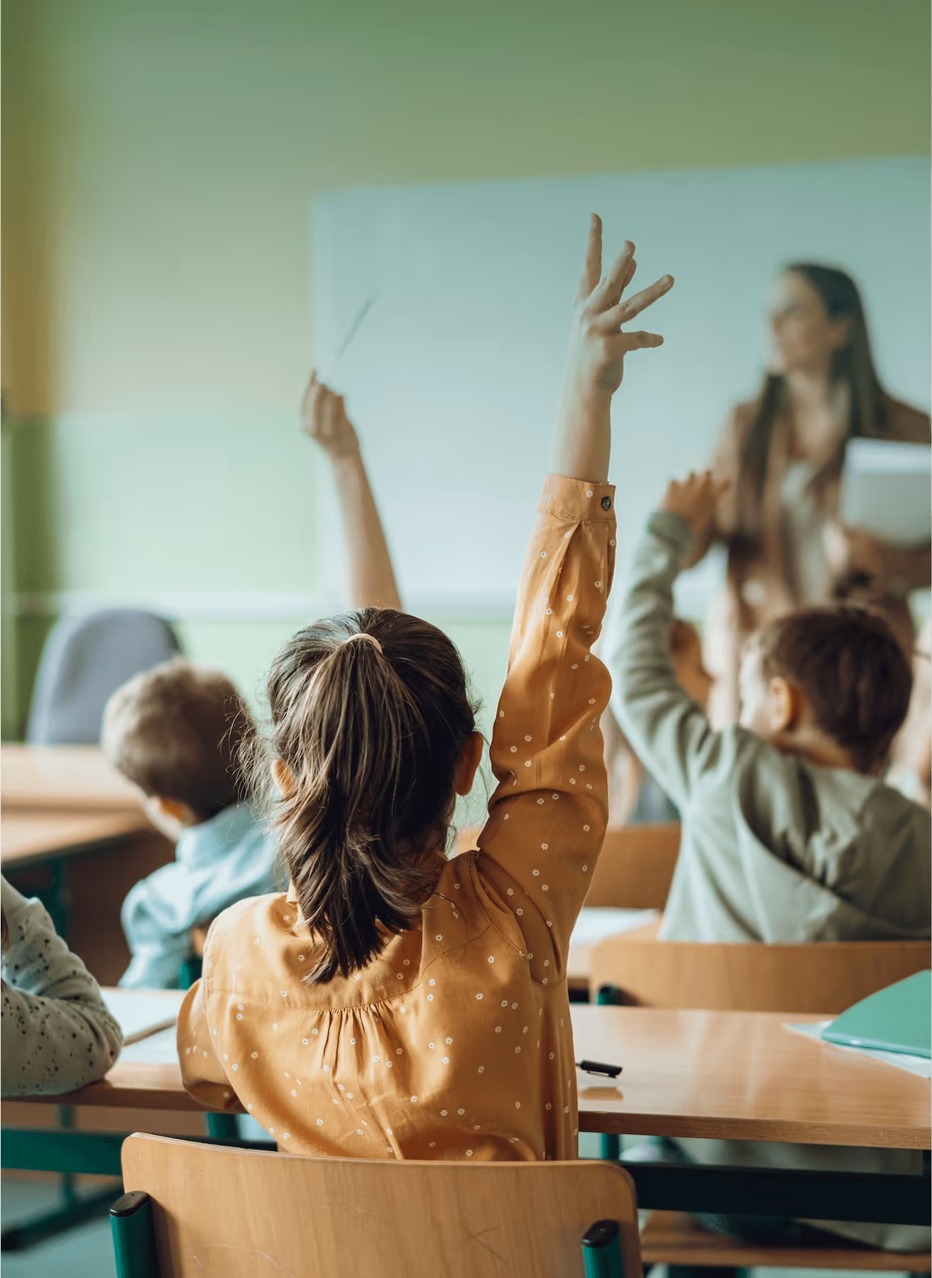 Children eagerly raising their hands in a classroom, seeking to answer questions from their teacher.