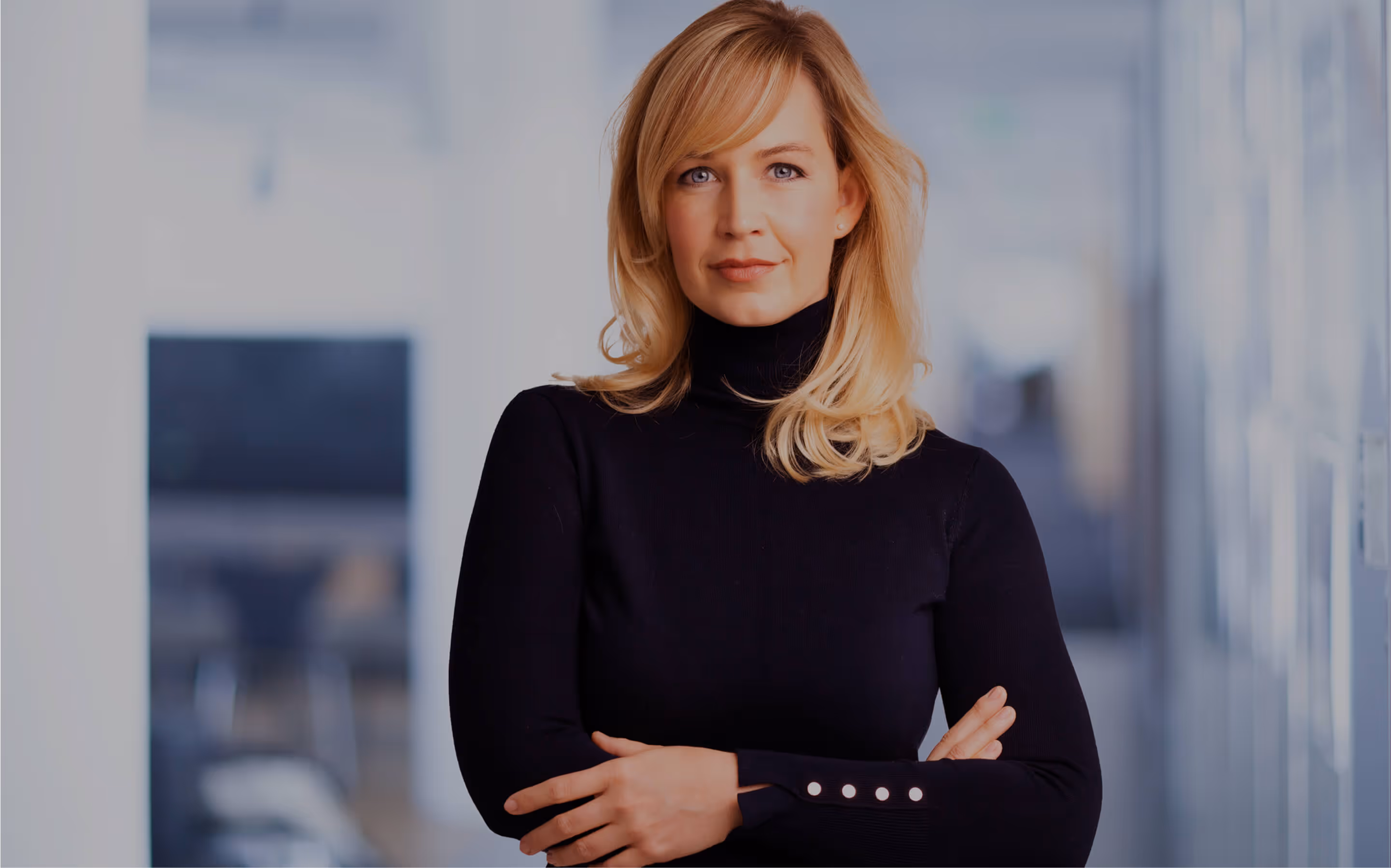 A woman wearing a black top is positioned in an office setting, surrounded by professional decor.