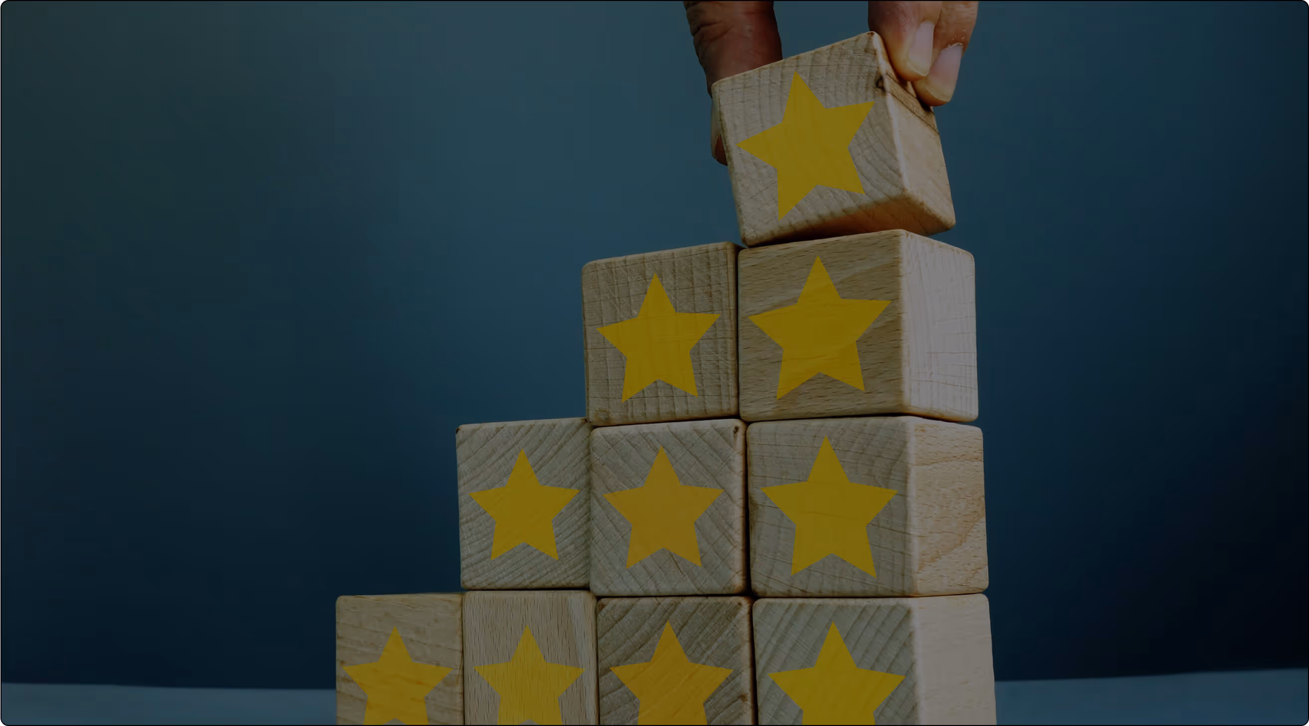 A hand places a wooden block with a yellow star on a pyramid made of similar star-marked blocks, against a blue background.