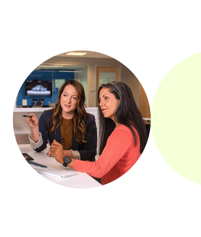 Zwei Frauen sitzen in einem Büro und besprechen gemeinsam etwas am Computer.