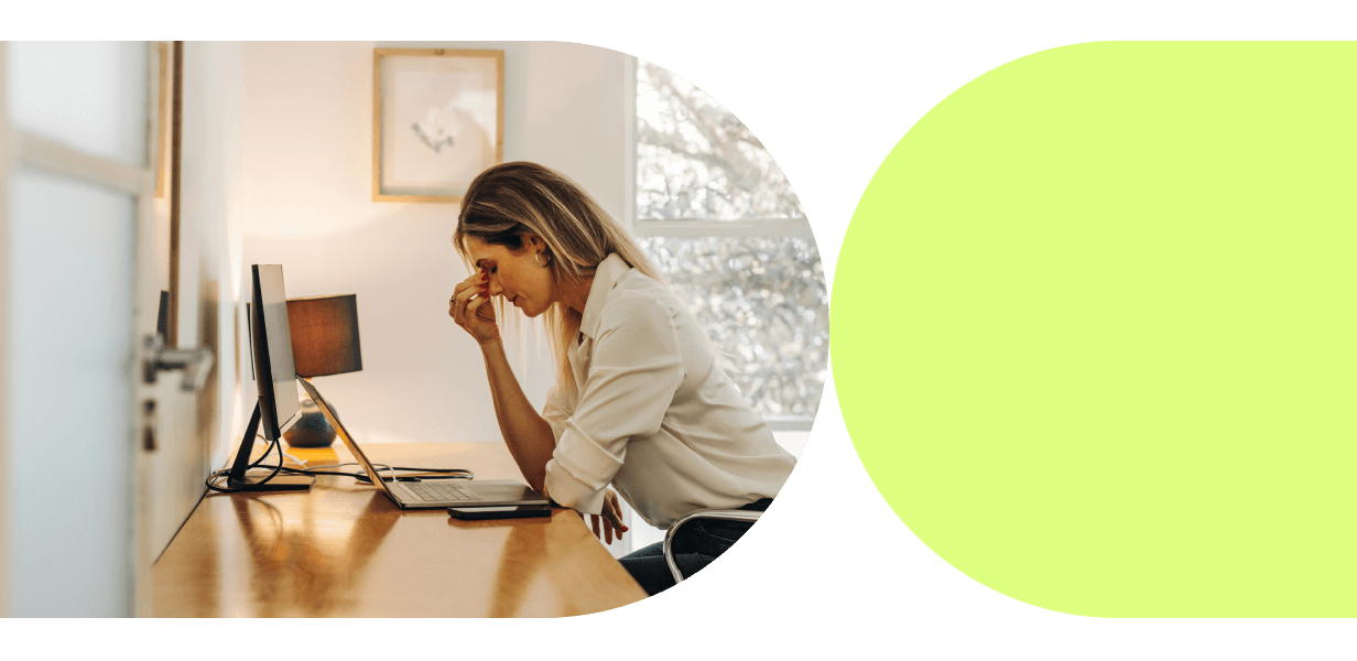 Frau sitzt erschöpft am Schreibtisch vor einem Laptop und reibt sich die Augen