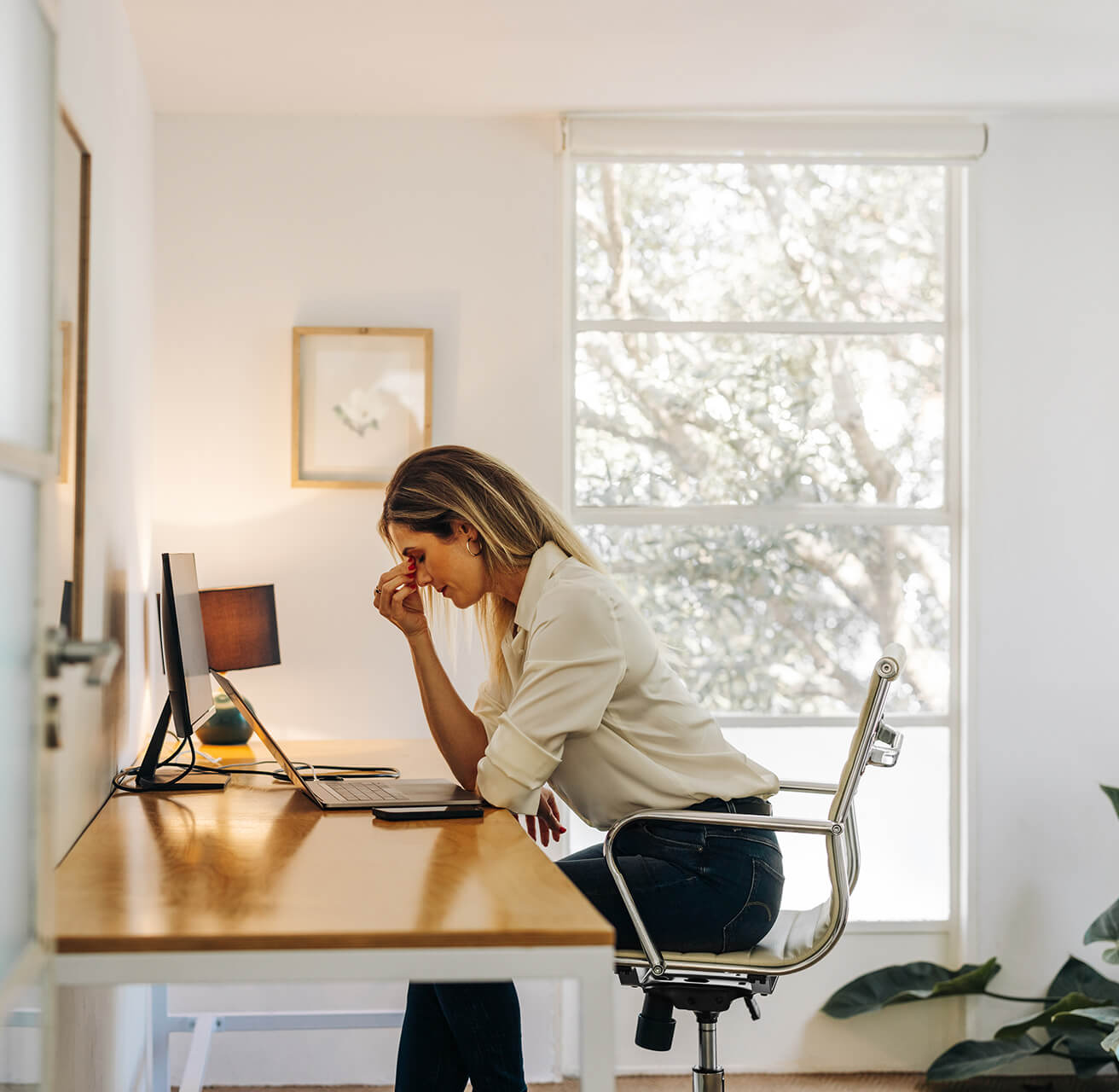 Gestresste Frau reibt sich erschöpft den Nasenrücken bei der Arbeit vor ihrem Laptop im Home-Office.