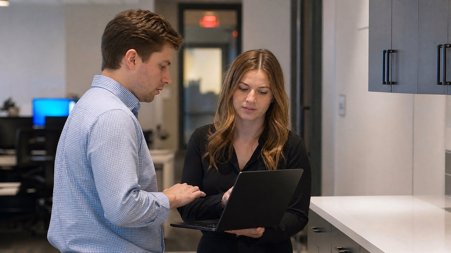 INFORMAL HUDDLE An IT professional  two people standing and talking near a ki