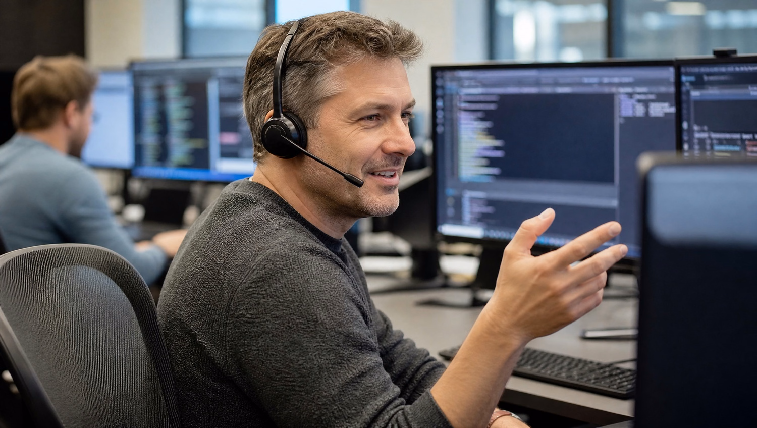 Support agent with headset speaks on phone at busy desk