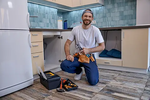 Man kneeling down to install a dishwasher with tools in front of him. 