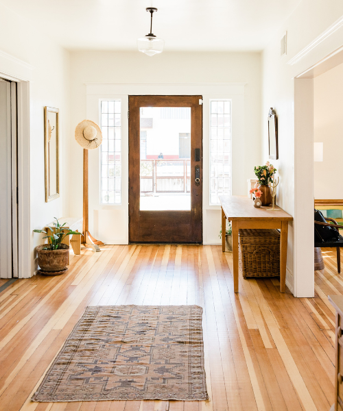 Bright entryway with wooden door, hardwood floors, and decorative rug