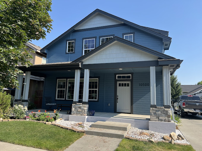 Blue two-story house with white trim, stone accents, and front garden
