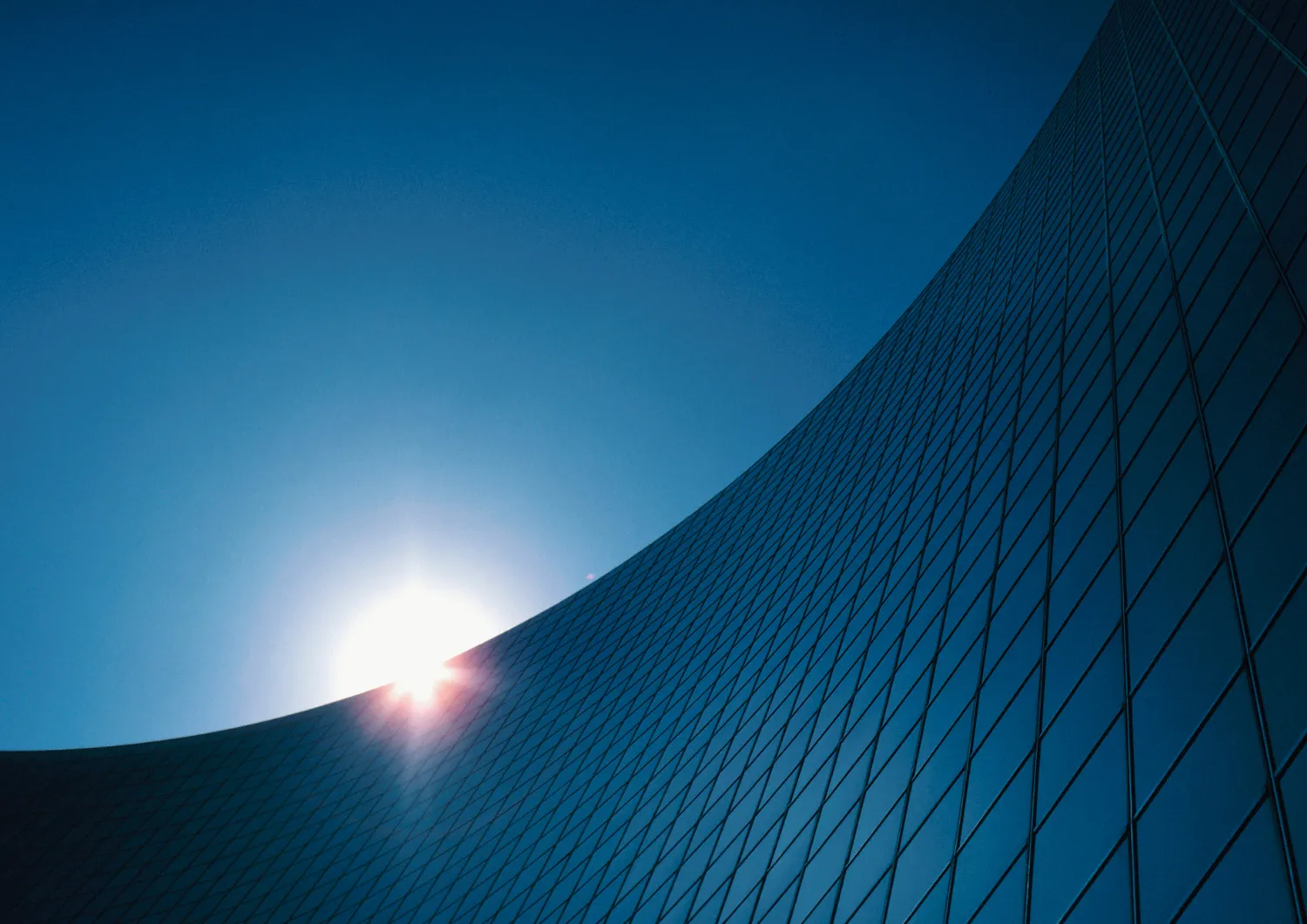 Sun setting behind a curved glass skyscraper.