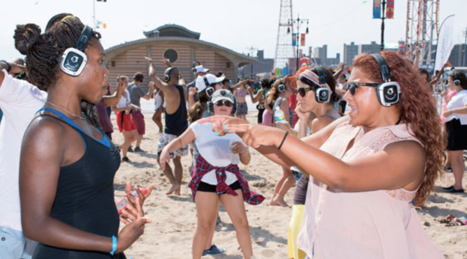 Beach Silent Disco - People joyfully enjoying the beach while wearing wireless headphones, creating a serene and immersive experience with the sound of the ocean in the background.