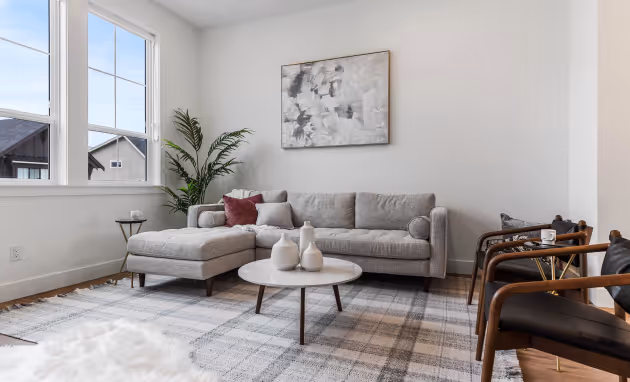Cedarbrook townhome living room with grey sectional couch up against the wall and a small marble coffee table in the center of the room, accompanied by a plaid grey and cream rug