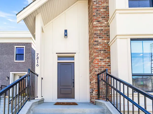 Wide grassy field with a small soccer goal and playground, houses in the background under a clear sky.