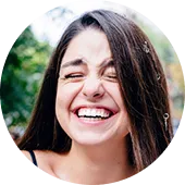 Young woman with long brown hair laughing joyfully outdoors.