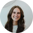 Smiling woman with long brown hair wearing a white top against a light background.